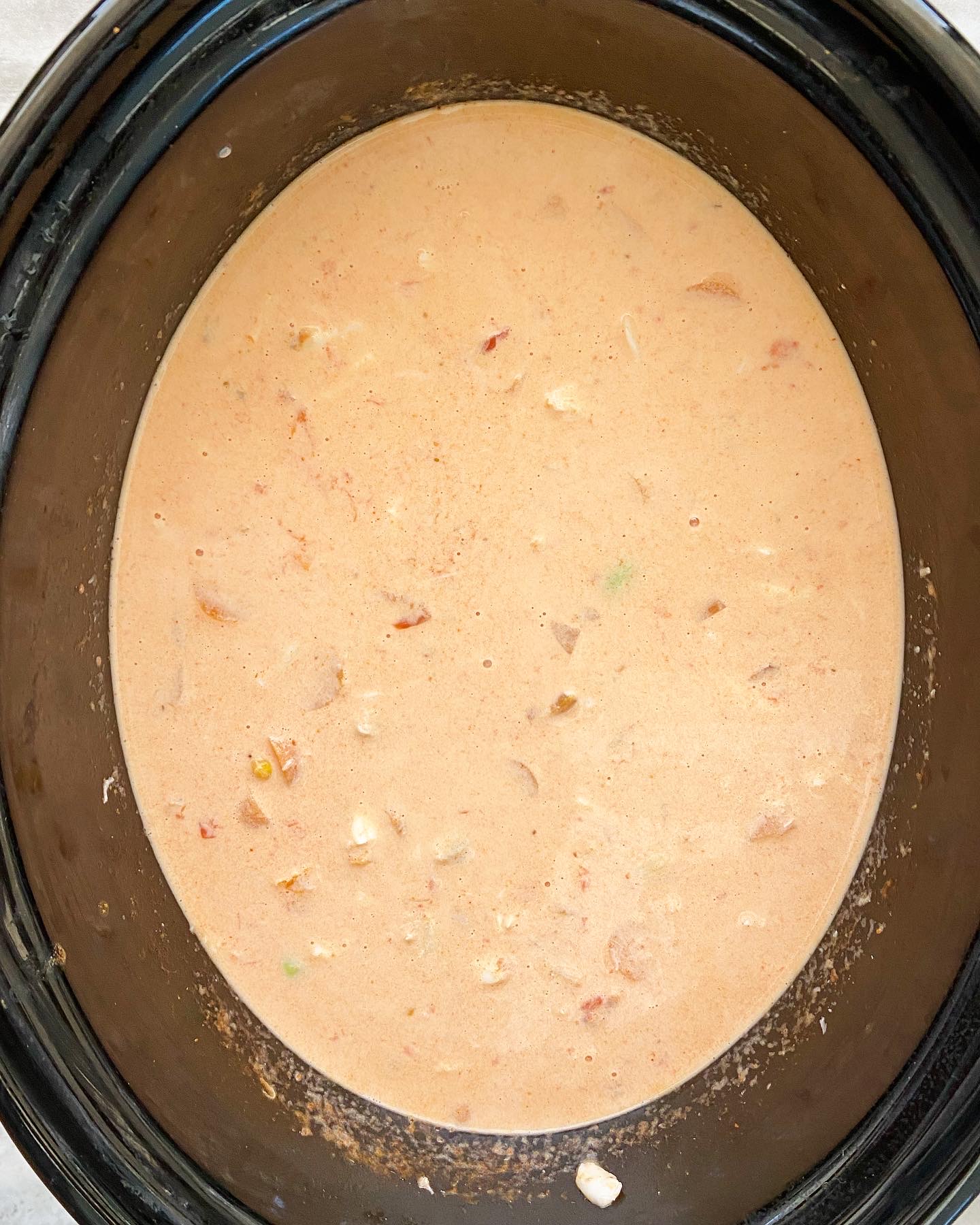 overhead shot of cooked crab soup in a black slow cooker with cream added