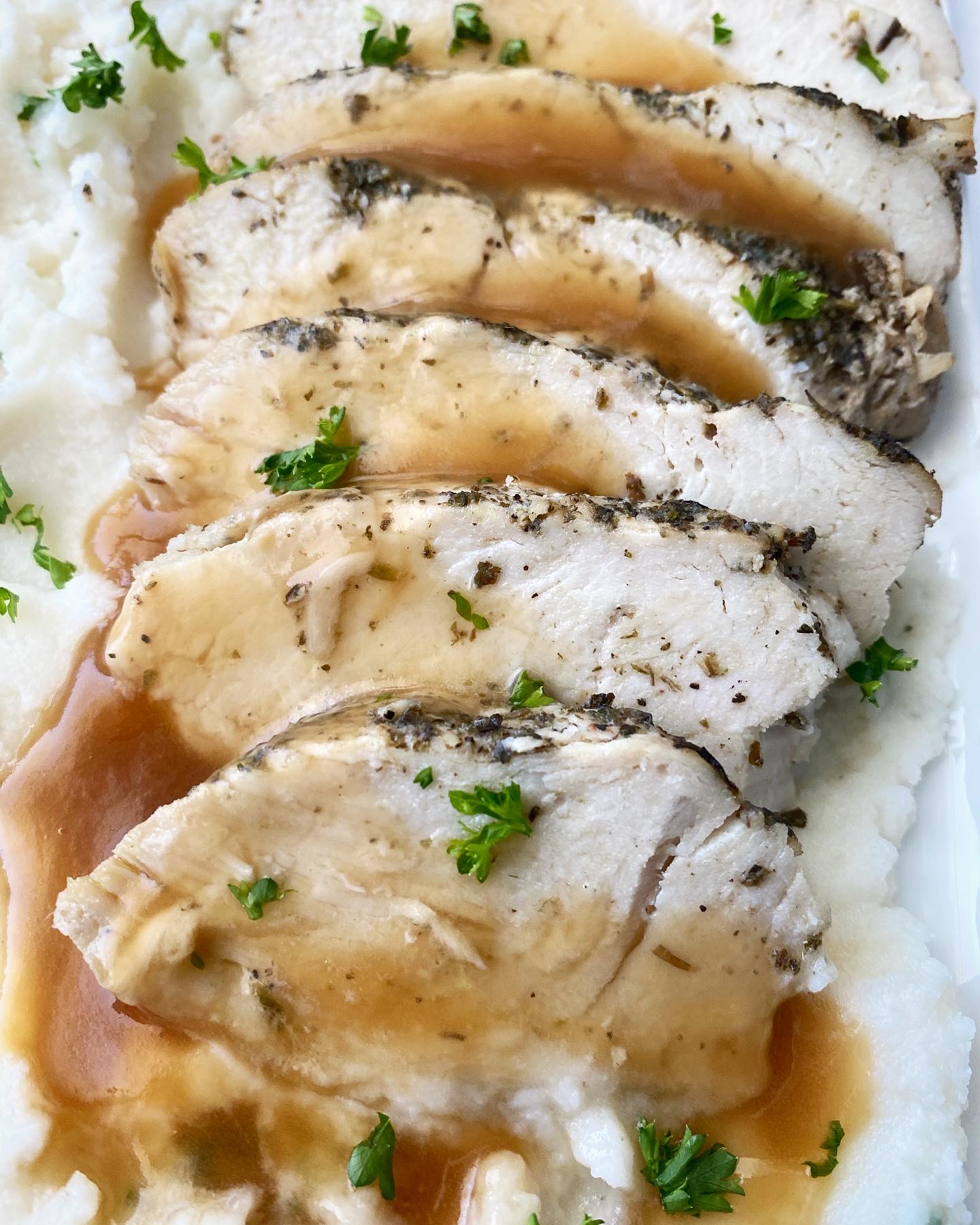 close up shot of crockpot turkey tenderloin over mashed potatoes on a white plate with gravy on top