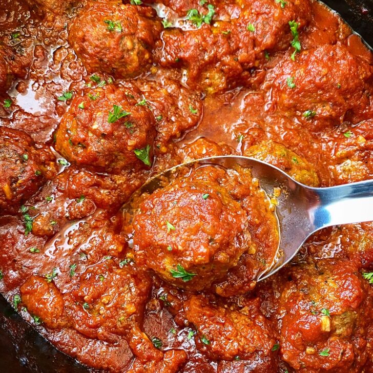 close up of slow cooker meatballs in a black crockpot on a silver spoon