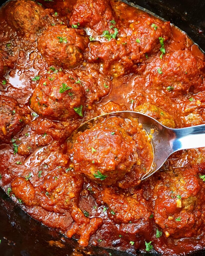 close up of slow cooker meatballs in a black crockpot on a silver spoon