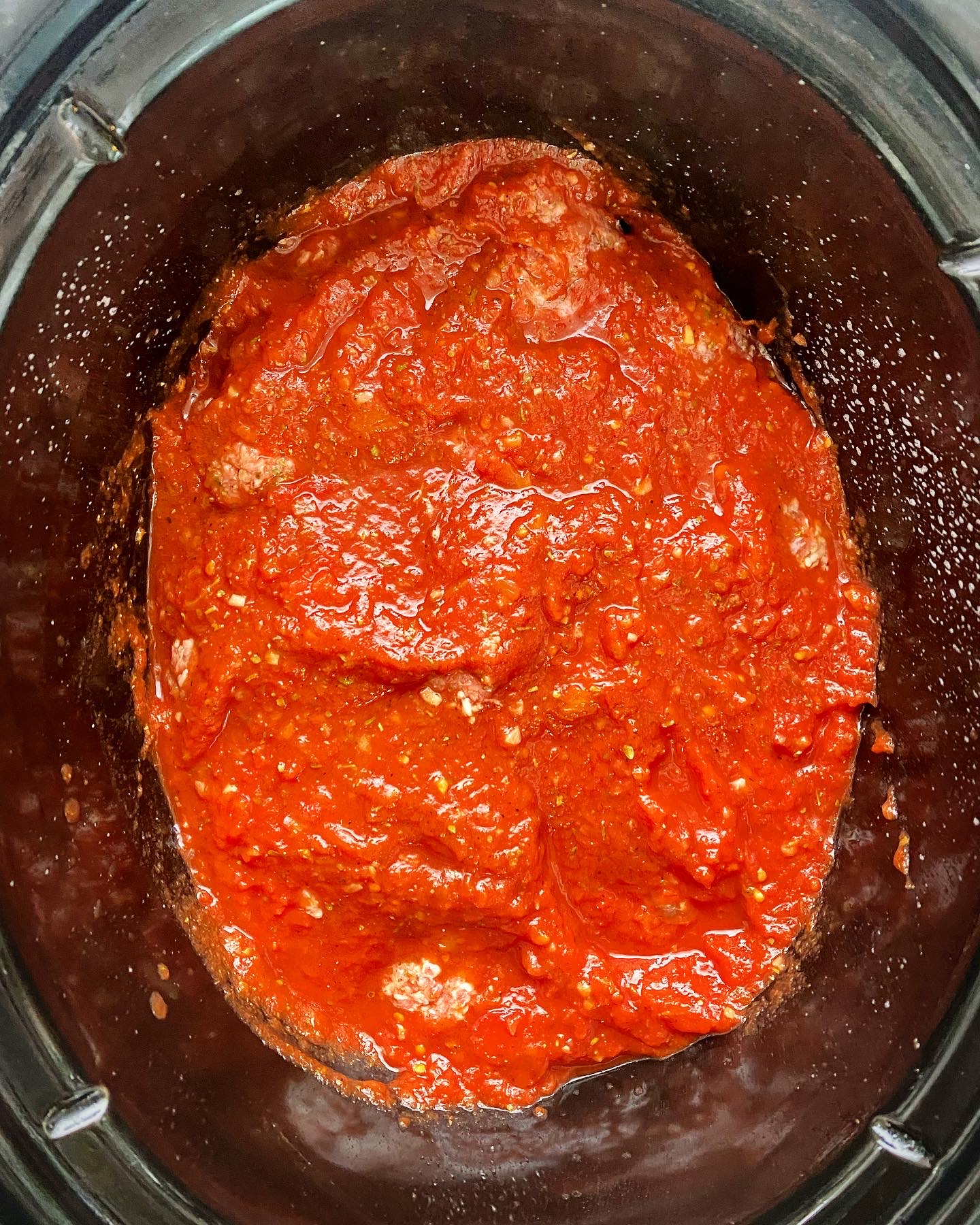 overhead shot of uncooked meatballs in a black crockpot with marinara sauce on top