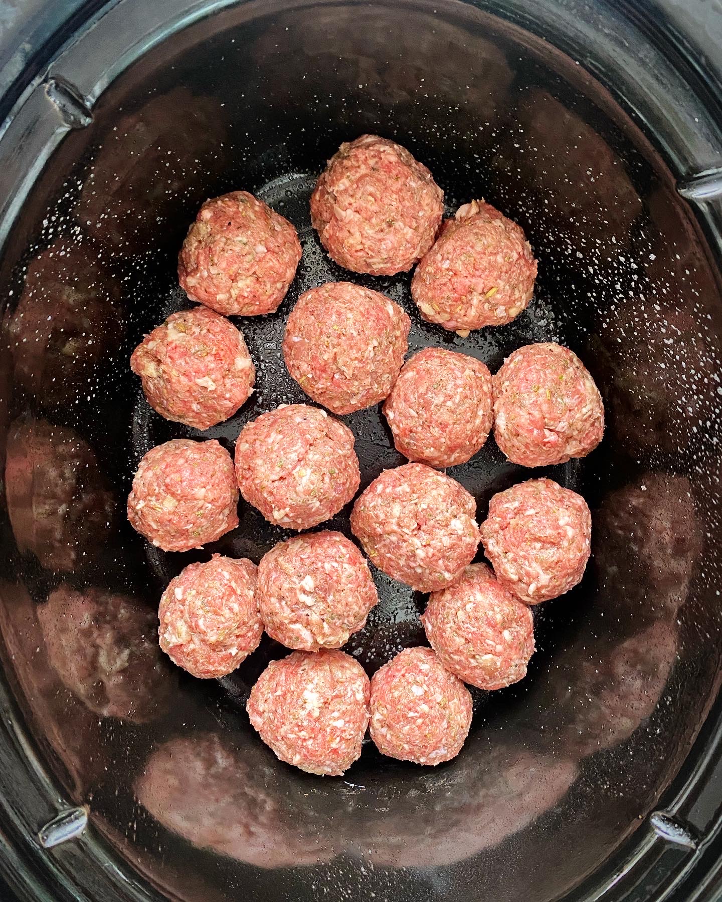 overhead shot of uncooked meatballs in a black crockpot