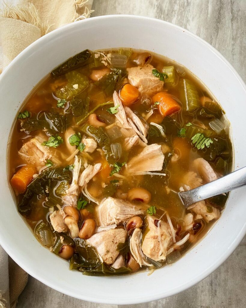 overhead shot of soul food soup in a white bowl with a silver spoon