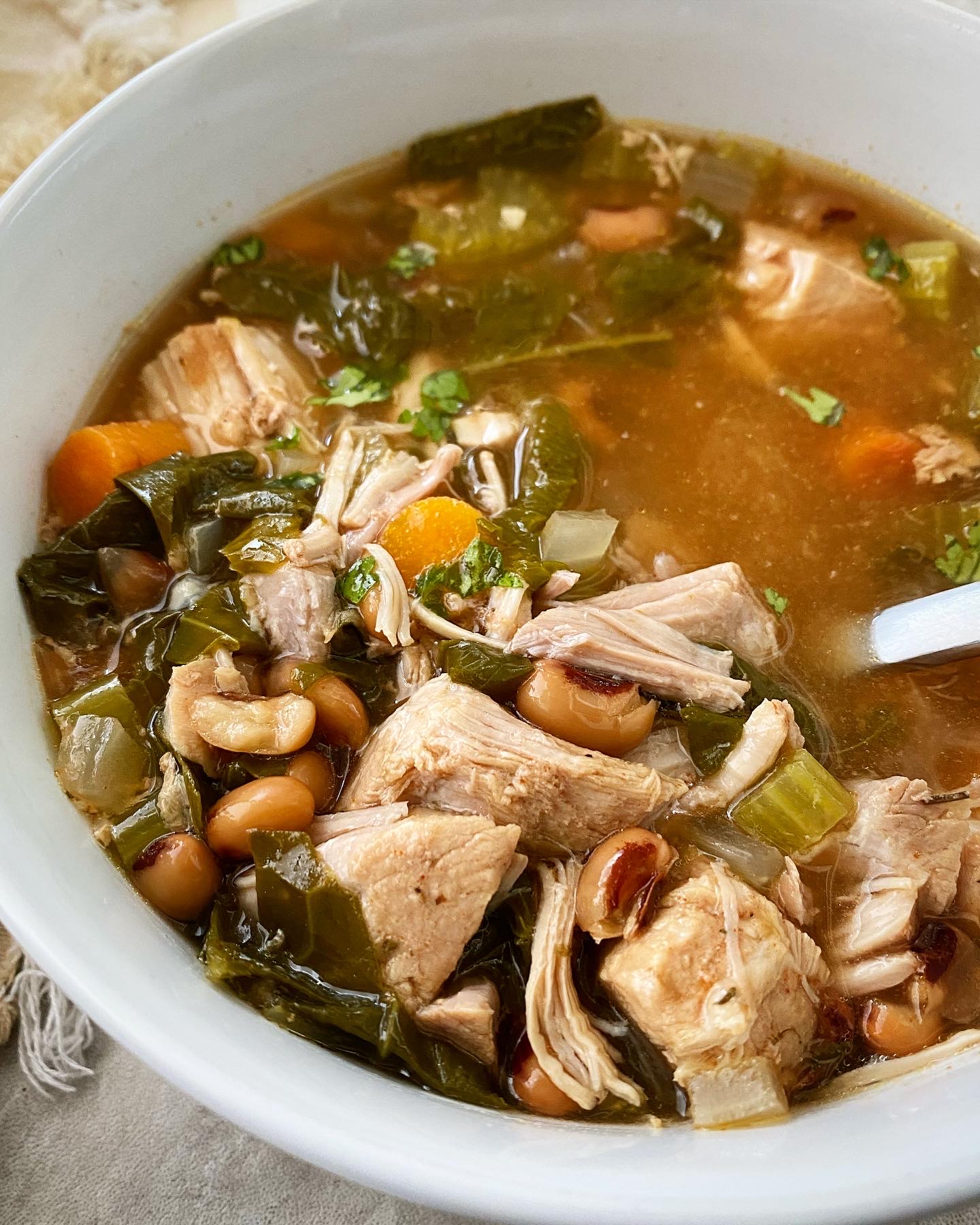 side close up shot of soul food soup in a white bowl with a silver spoon