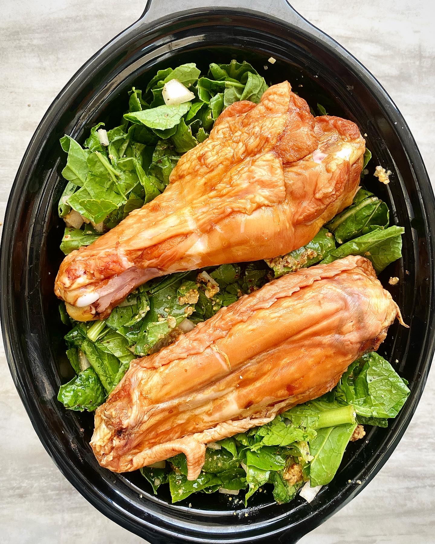 overhead shot of uncooked greens with a smoked turkey wings on top in a black slow cooker