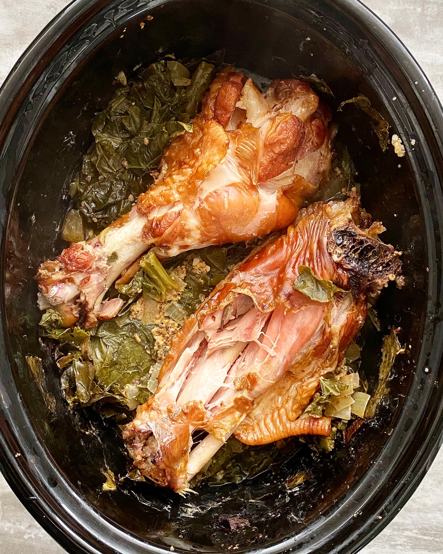 overhead shot of cooked greens with a smoked turkey wings on top in a black slow cooker