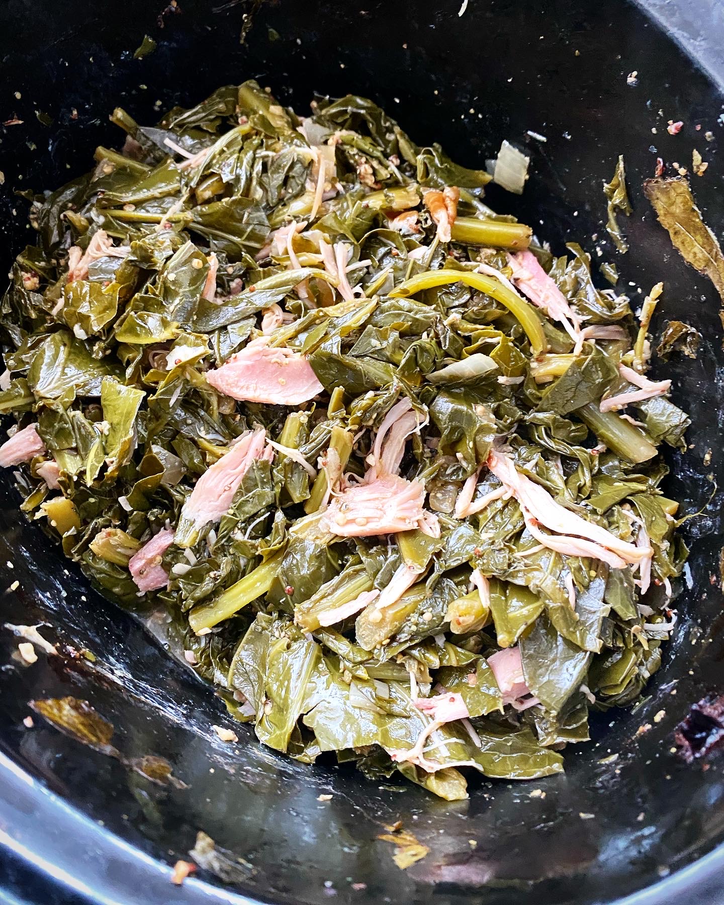 overhead shot of cooked greens with smoked turkey in a black slow cooker