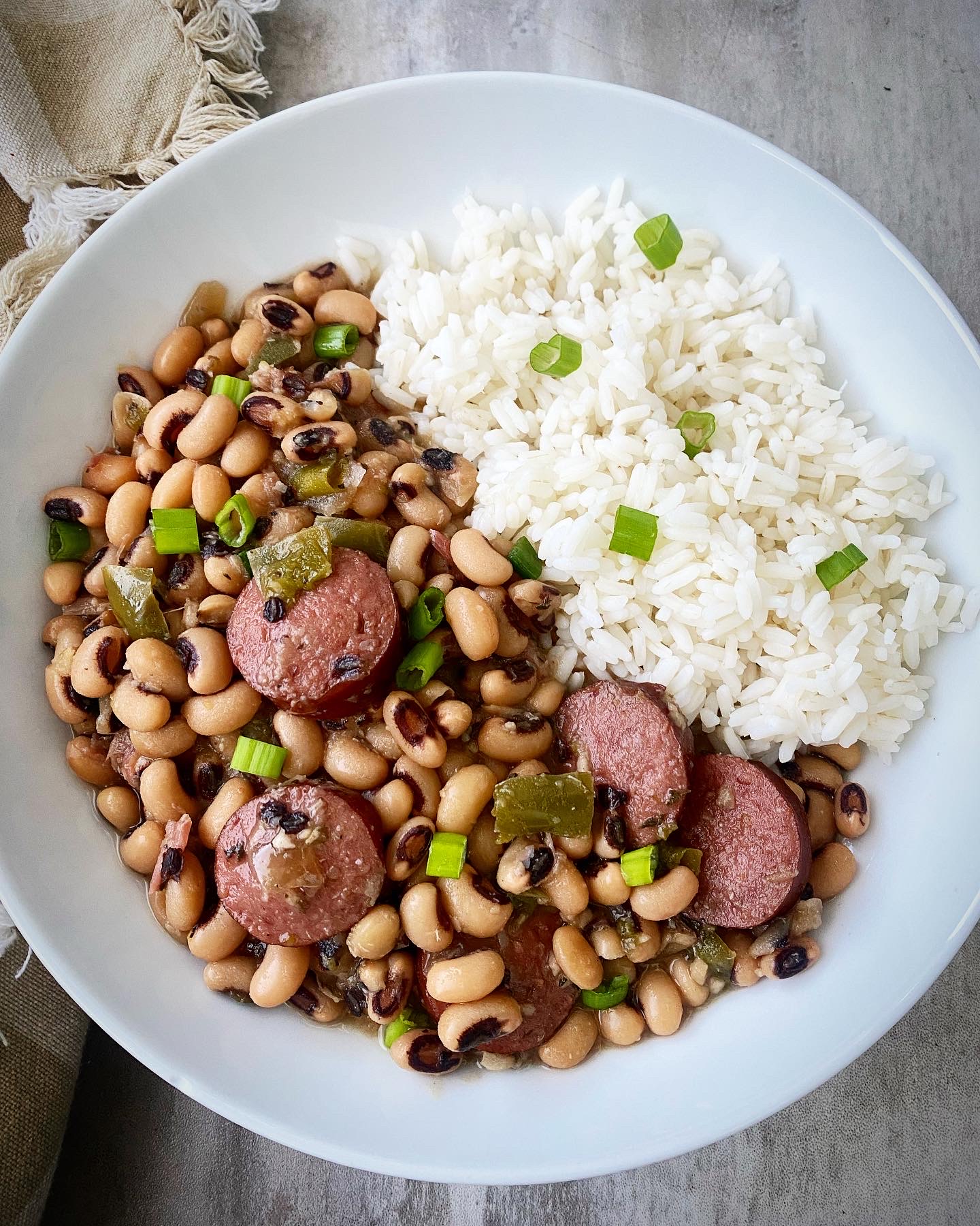 overhead shot of hoppin john served with white rice in a white bowl, garnished with green onions