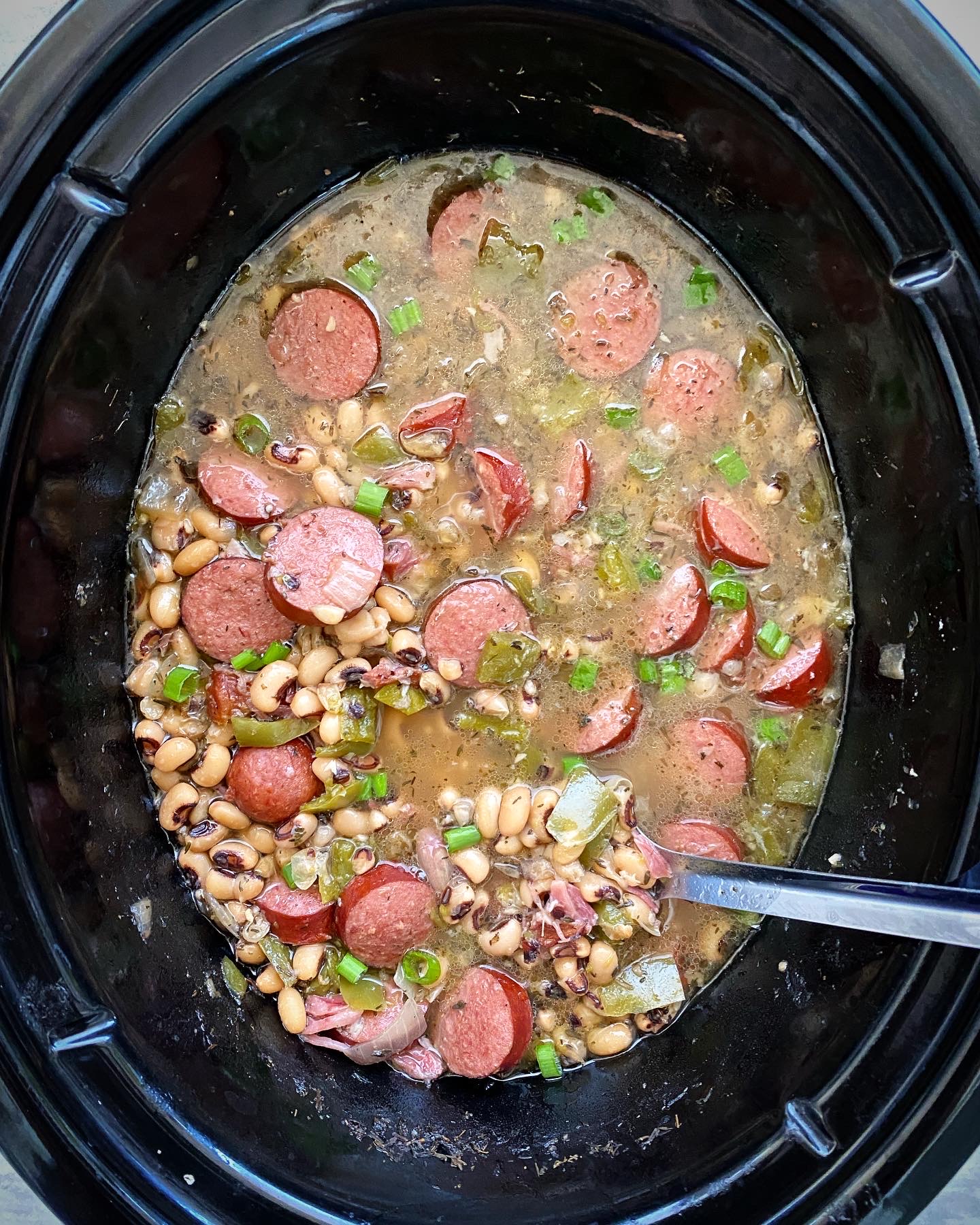overhead shot of cooked hoppin john in a black slow cooker with a silver spoon
