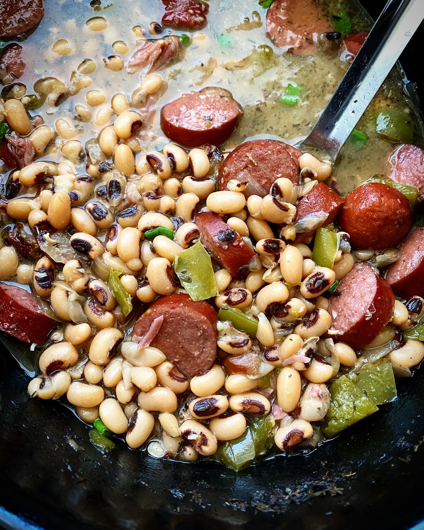 close up shot of cooked hoppin john in a black slow cooker with large silver spoon