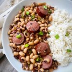 overhead shot of hoppin john served with white rice in a white bowl, garnished with green onions with a silver fork