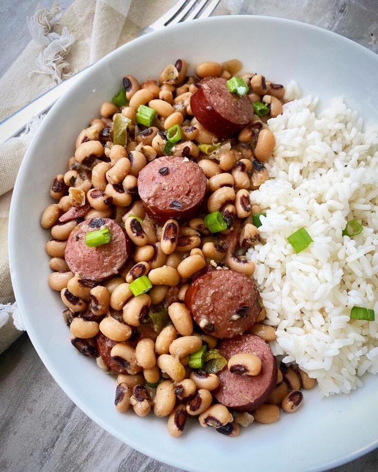 overhead shot of hoppin john served with white rice in a white bowl, garnished with green onions with a silver fork