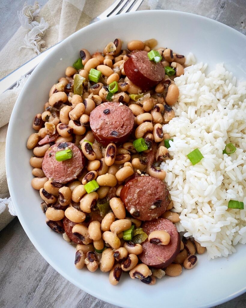 overhead shot of hoppin john served with white rice in a white bowl, garnished with green onions with a silver fork