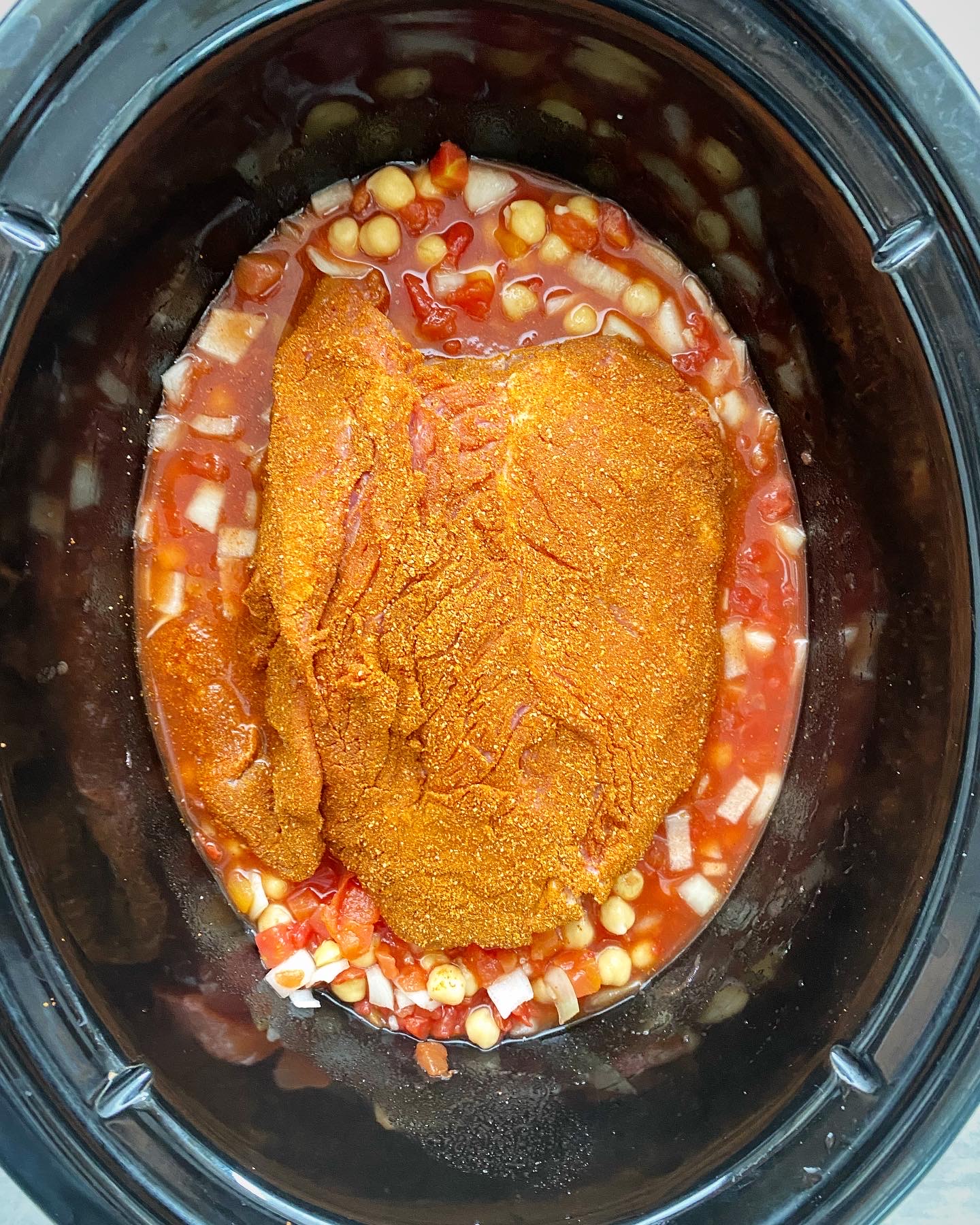 overhead shot of uncooked north african lamb in a black slow cooker