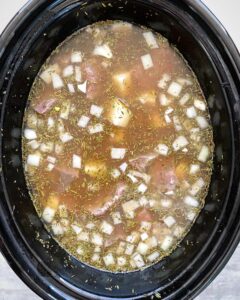 overhead shot of uncooked steak & potato soup in a black slow cooker