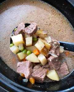 overhead shot of cooked steak & potato soup in a black slow cooker