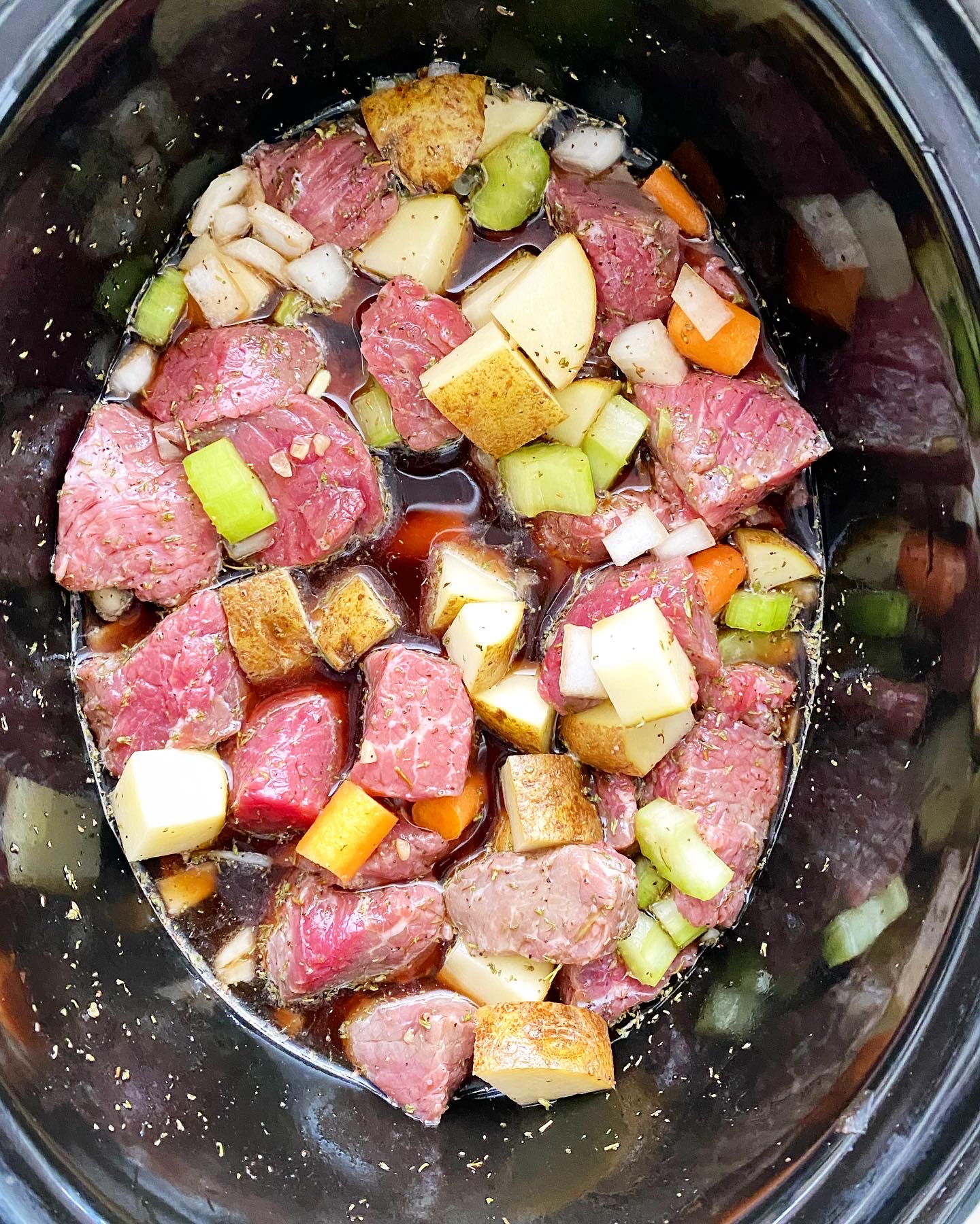 overhead shot of uncooked Guinness beef stew in a black slow cooker