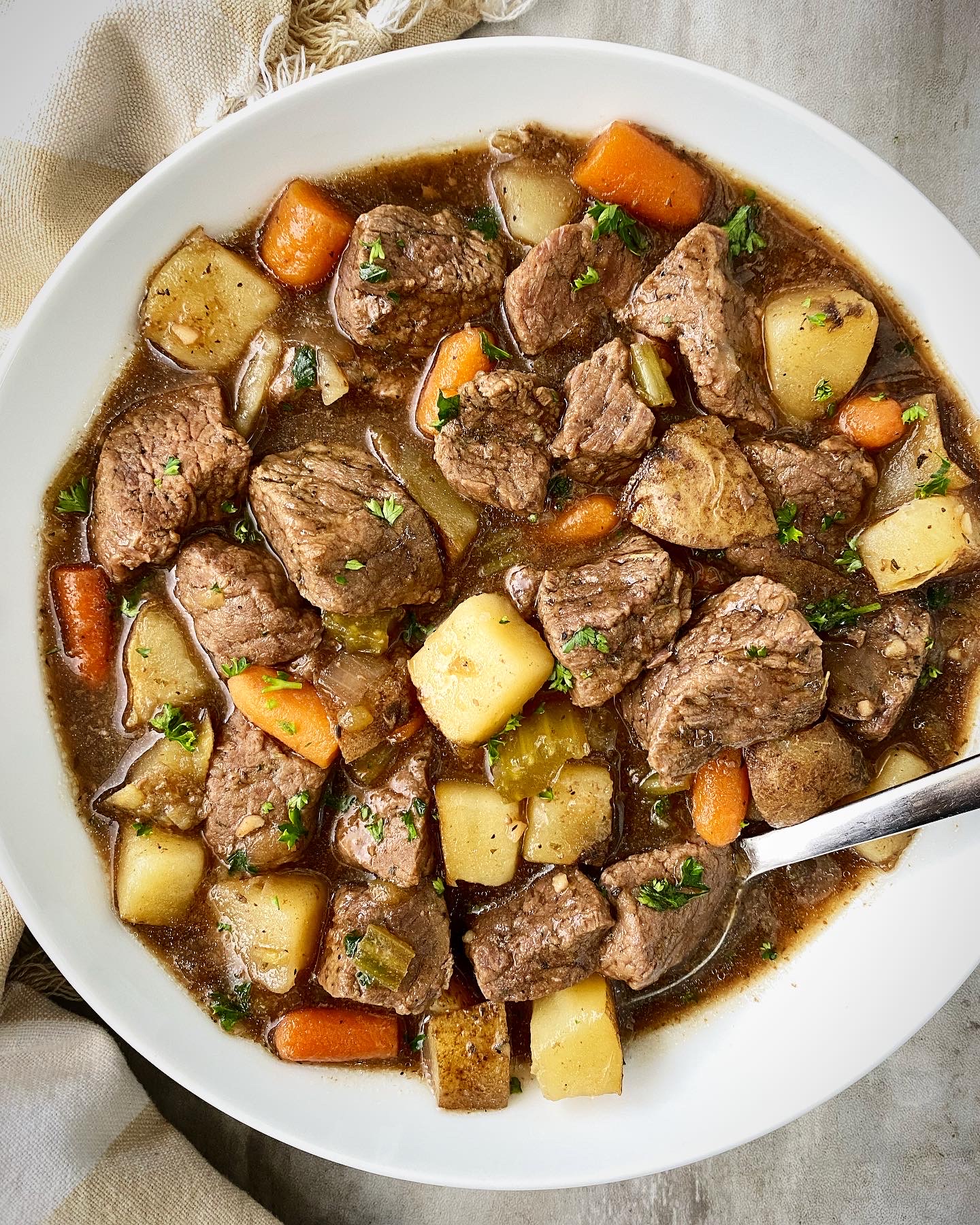 overhead shot of cooked Guinness beef stew in a white bowl with a silver spoon