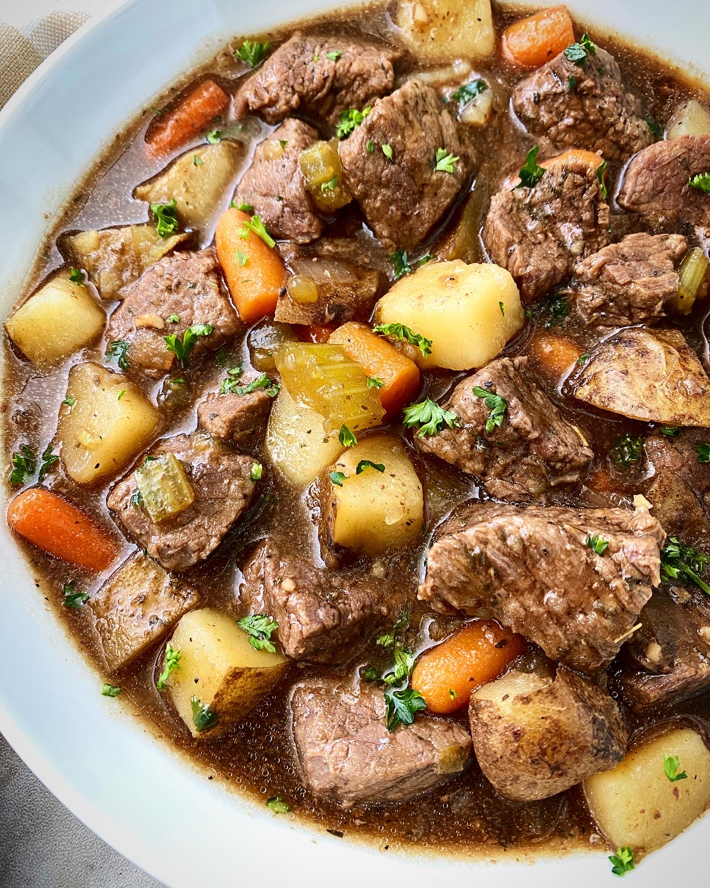 close up shot of cooked Guinness beef stew in a white bowl with a silver spoon