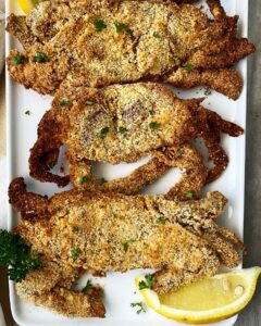 over head shot of cooked air fryer crabs on a white plate garnished with parsley & lemon wedges
