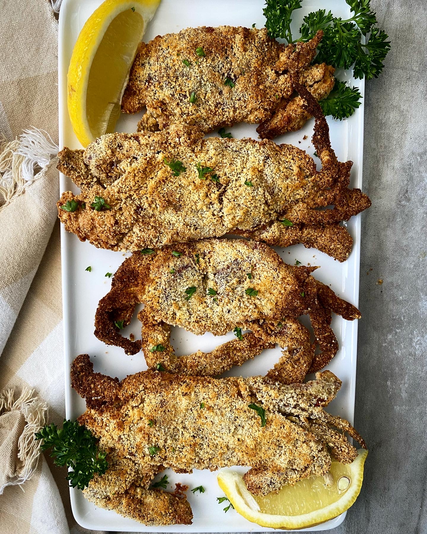 over head shot of cooked air fryer crabs on a white plate garnished with parsley & lemon wedges
