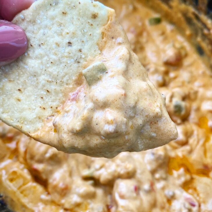 close up shot of a chip dipped in beef queso dip over a black slow coooker
