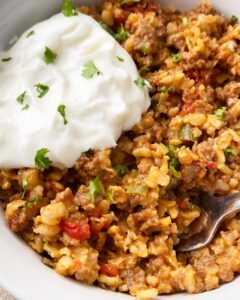 overhead shot of cooked ground beef spanish rice in a white bowl with sour cream