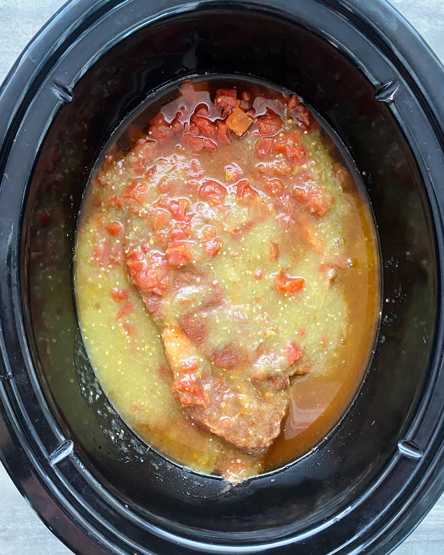 overhead shot of uncooked salsa verde beef in a black slow cooker