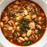 overhead shot of cooked sausage white bean soup in a white bowl