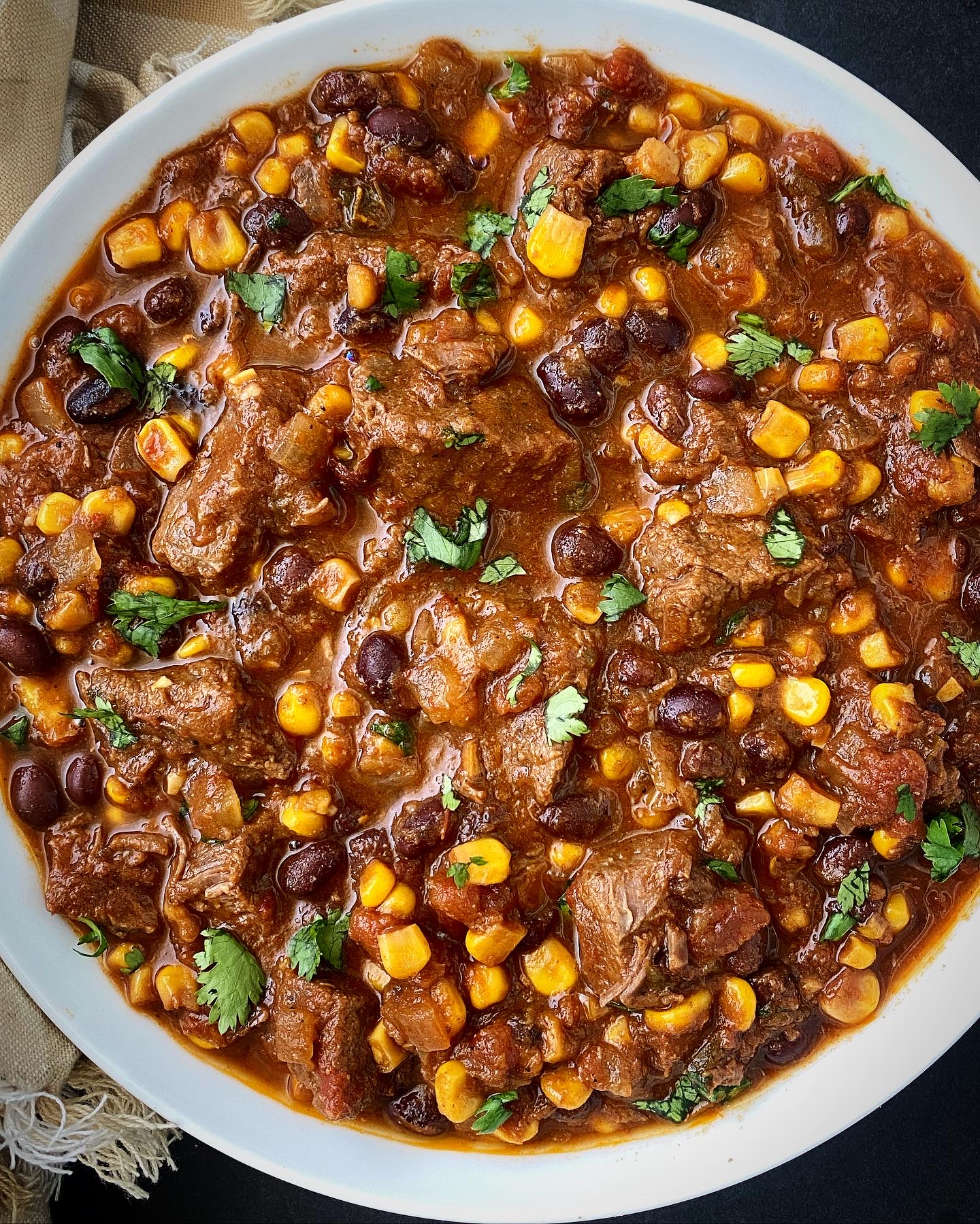overhead shot of cooked salsa beef stew in a white bowl garnished with fresh cilantro