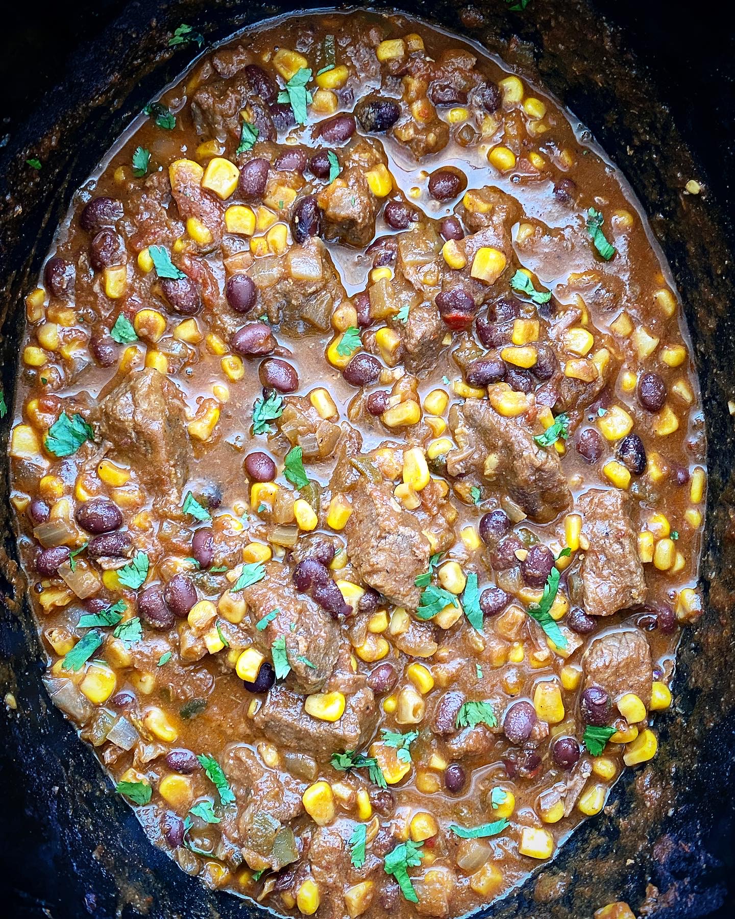 overhead shot of cooked salsa beef stew in a black slow cooker garnished with fresh cilantro