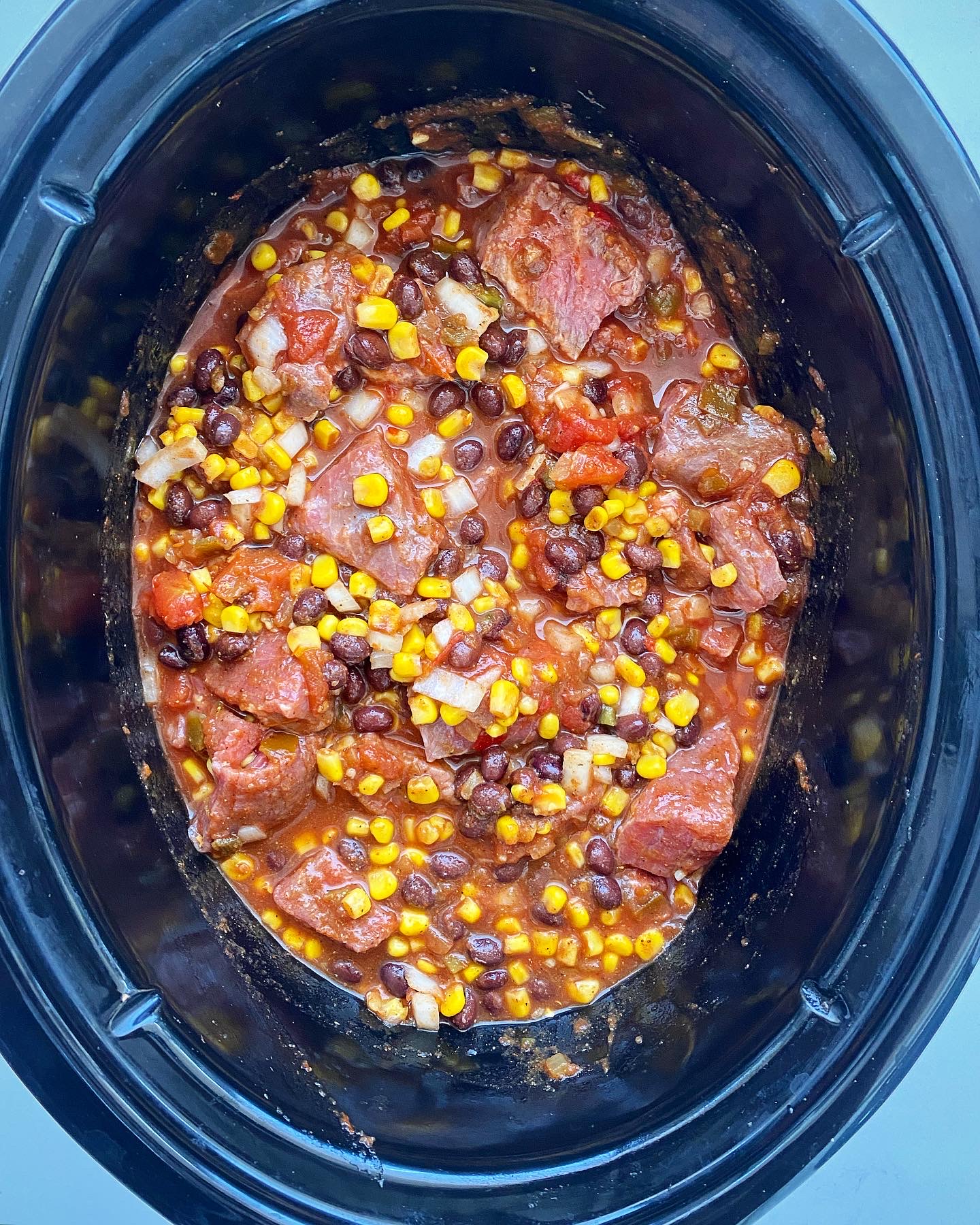 overhead shot of uncooked salsa beef stew in a black slow cooker 