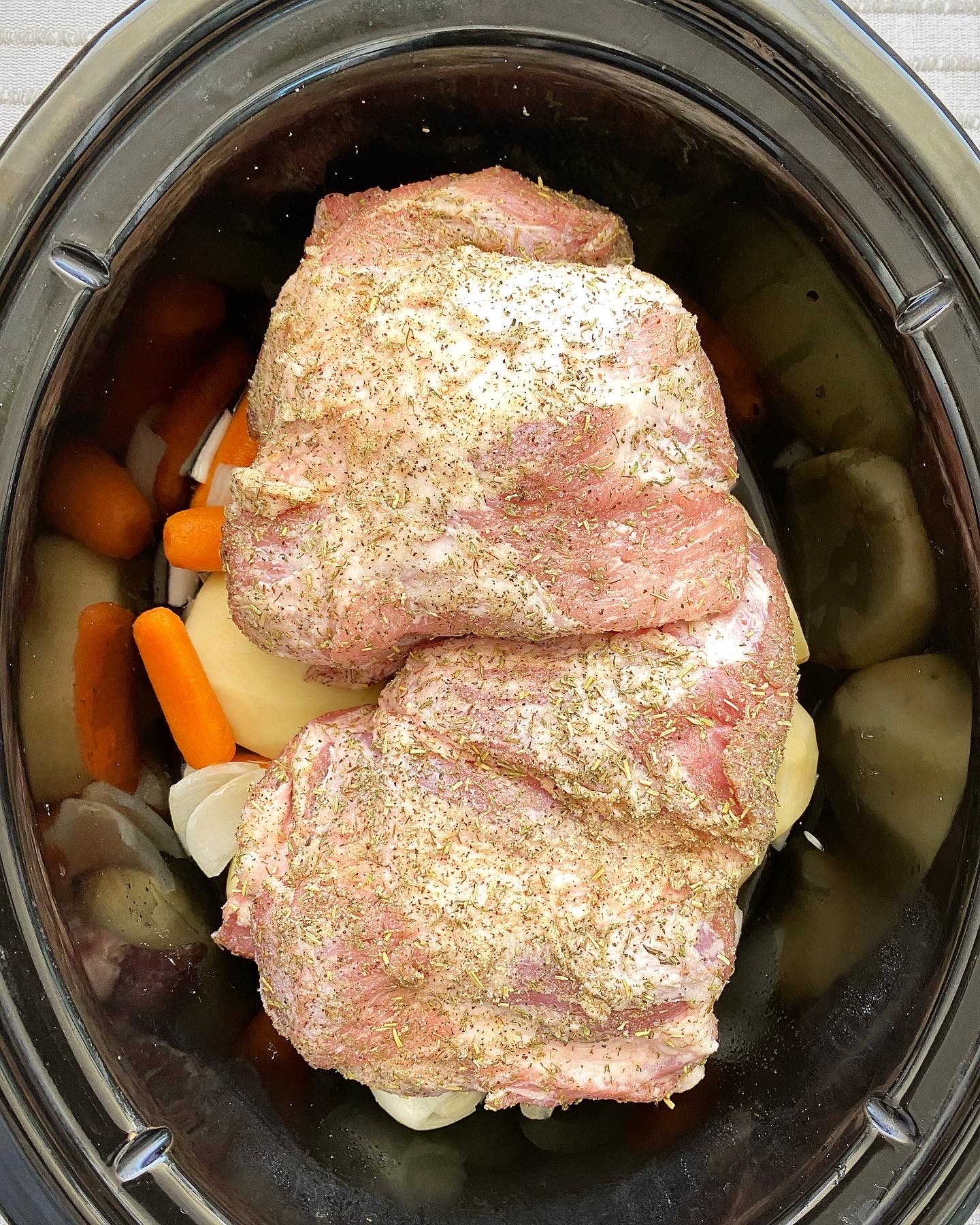 overhead shot of uncooked crockpot roast pork in a black slow cooker