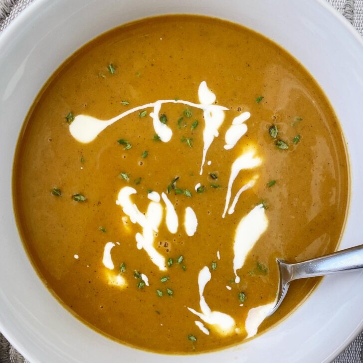 overhead shot of pumpkin bisque in a white bowl garnished with fresh thyme and a drizzle of coconut milk