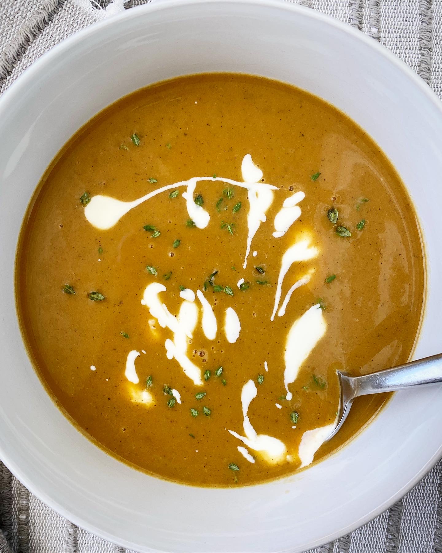 overhead shot of pumpkin bisque in a white bowl garnished with fresh thyme and a drizzle of coconut milk