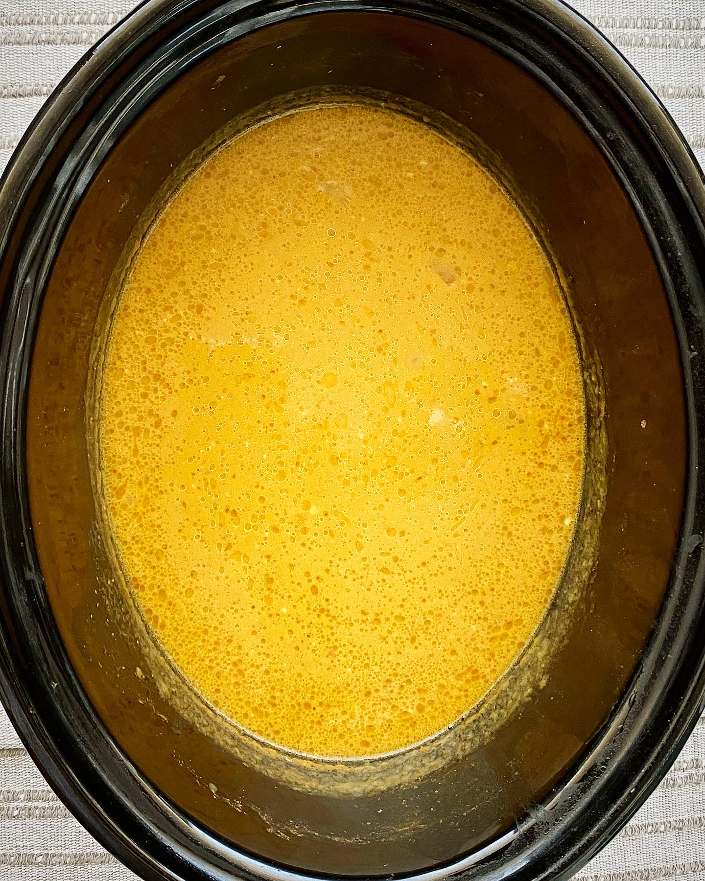 overhead shot of cooked crockpot pumpkin bisque in a black slow cooker