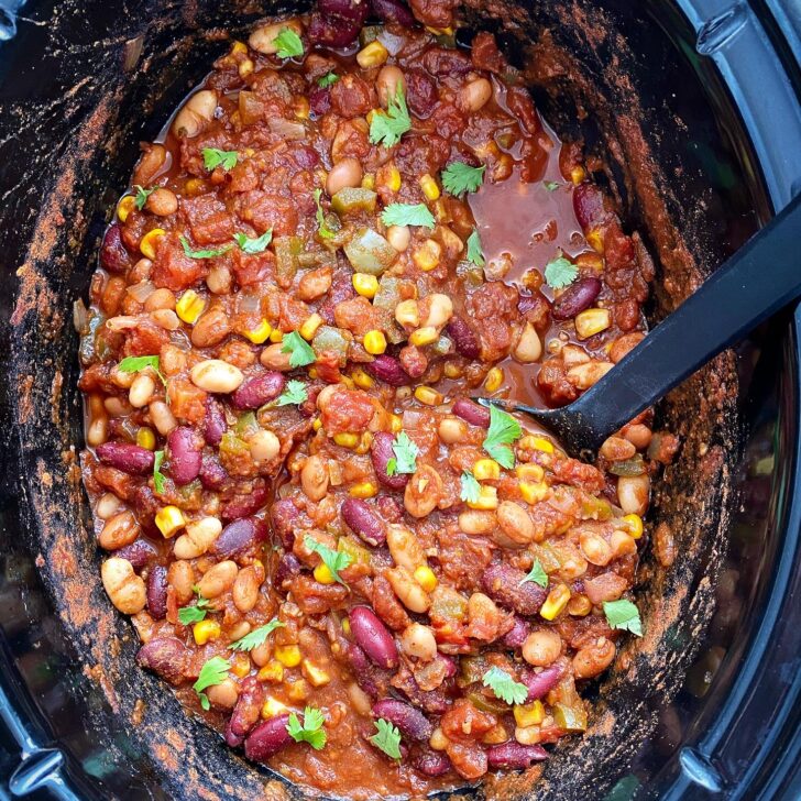 overhead shot of cooked the best crockpot vegan chili in a black slow cooker garnished with cilantro