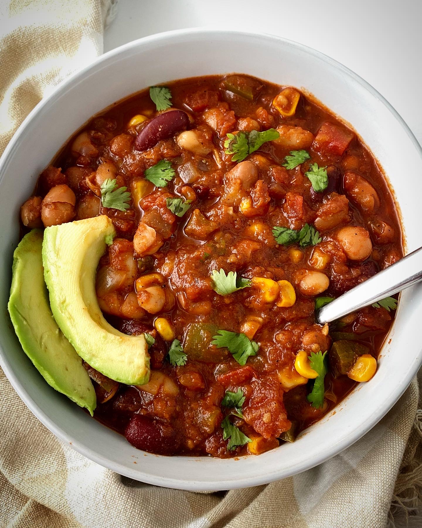 overhead shot of cooked best crockpot vegan chili in a white bowl garnished with cilantro and sliced avocado
