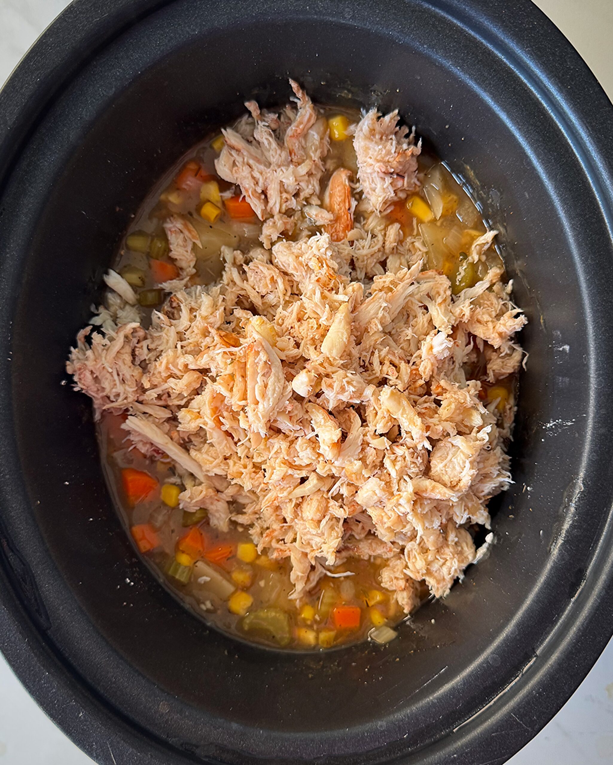 overhead shot of cooked Corn And Crab Chowder in a black slow cooker with a oile of crab added on top