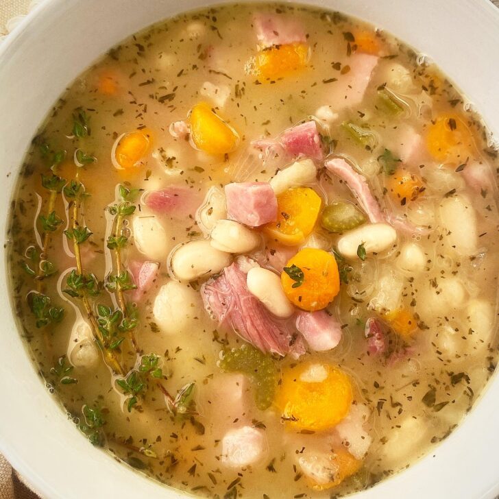 close up shot of slow cooker ham and bean soup in a white bowl garnished with fresh thyme