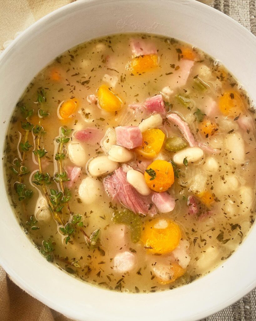 close up shot of slow cooker ham and bean soup in a white bowl garnished with fresh thyme