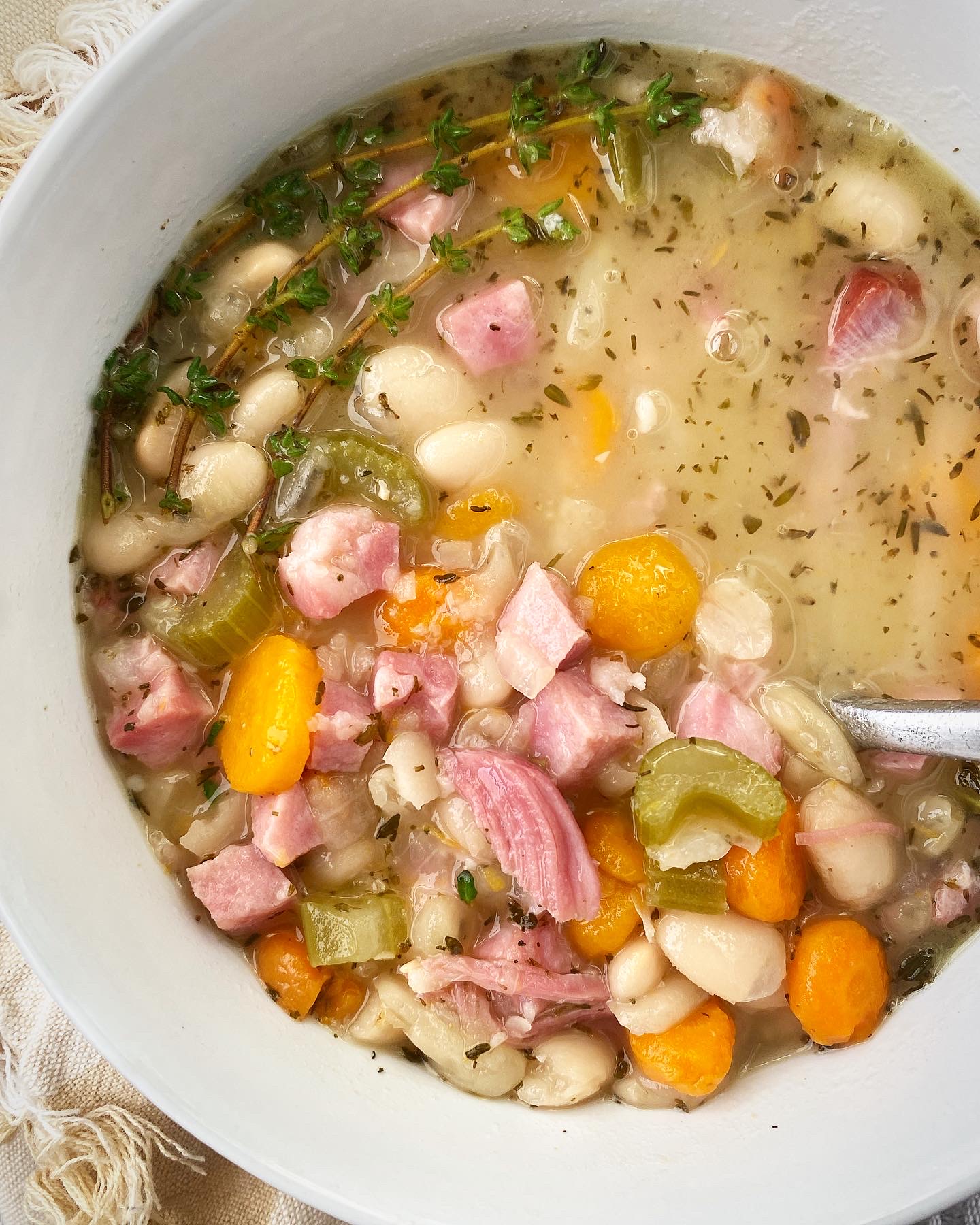 close up shot of slow cooker ham and bean soup in a white bowl garnished with fresh thyme