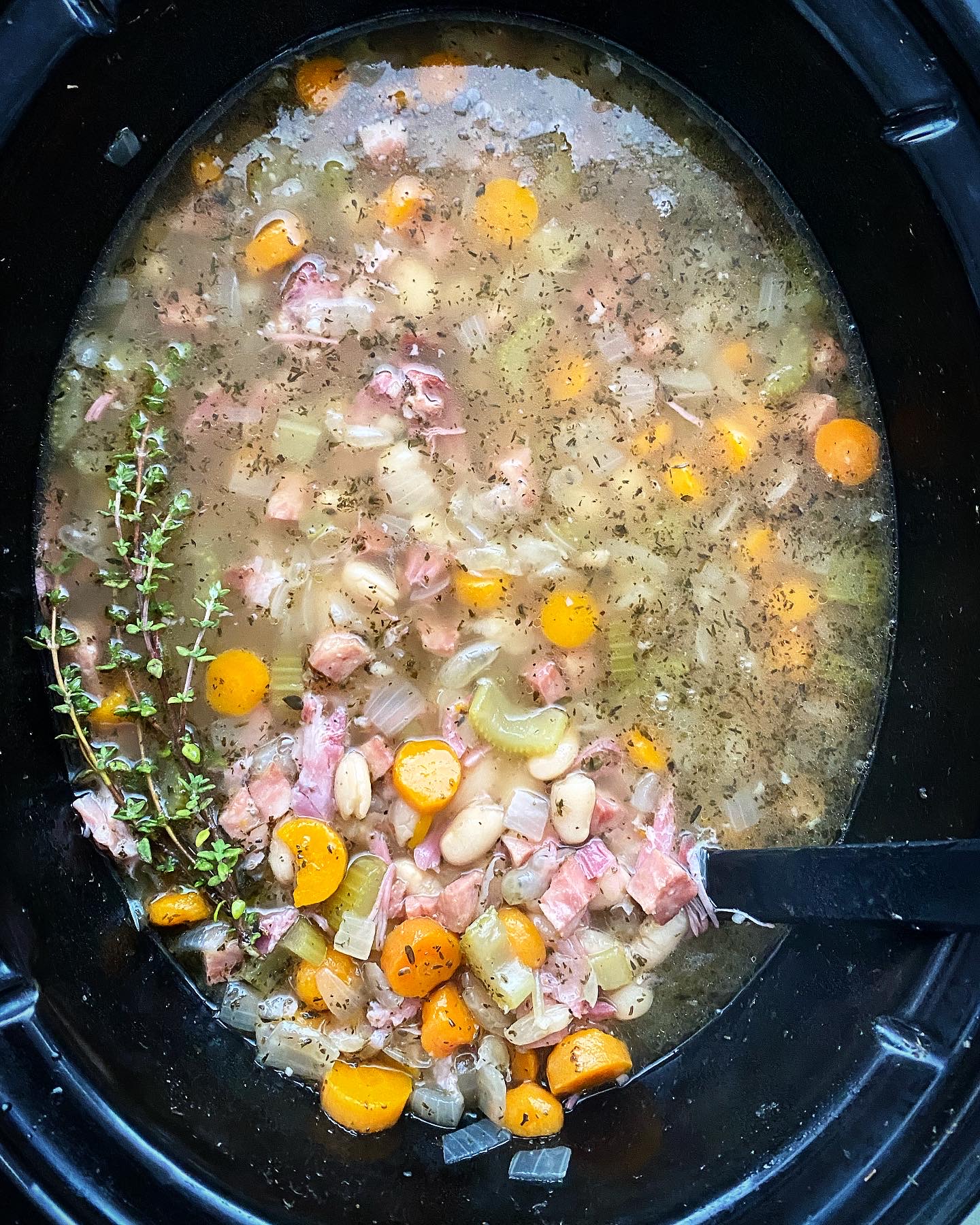overhead shot of cooked crockpot ham and bean soup in a black slow cooker garnished with fresh thyme