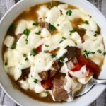 overhead shot of slow cooker cheesesteak soup in a white bowl with melted provolone cheese on top