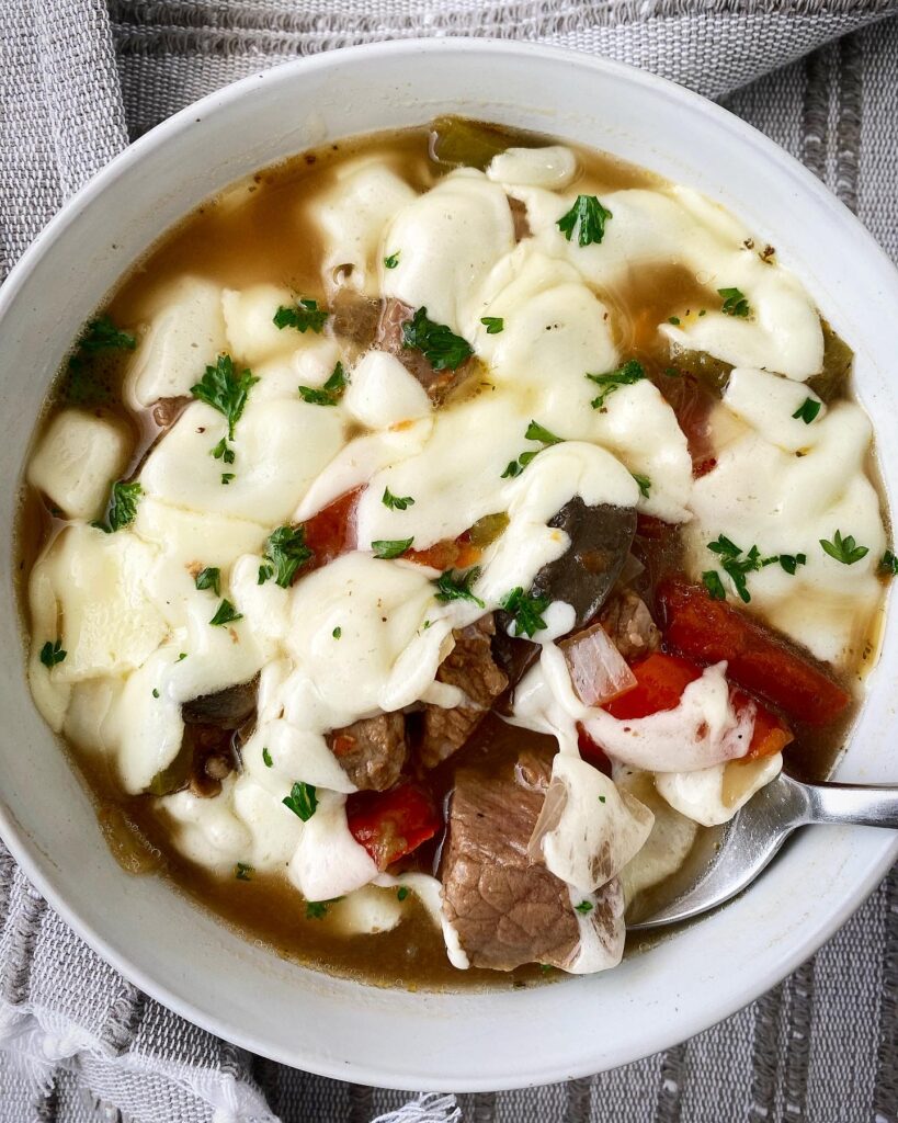 overhead shot of slow cooker cheesesteak soup in a white bowl with melted provolone cheese on top