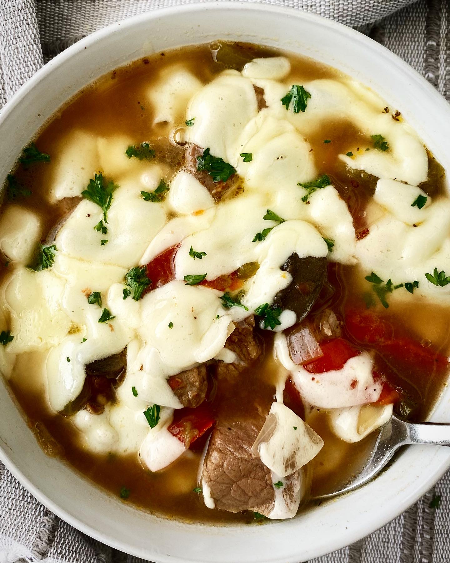 overhead shot of slow cooker cheesesteak soup in a white bowl with melted provolone cheese on top