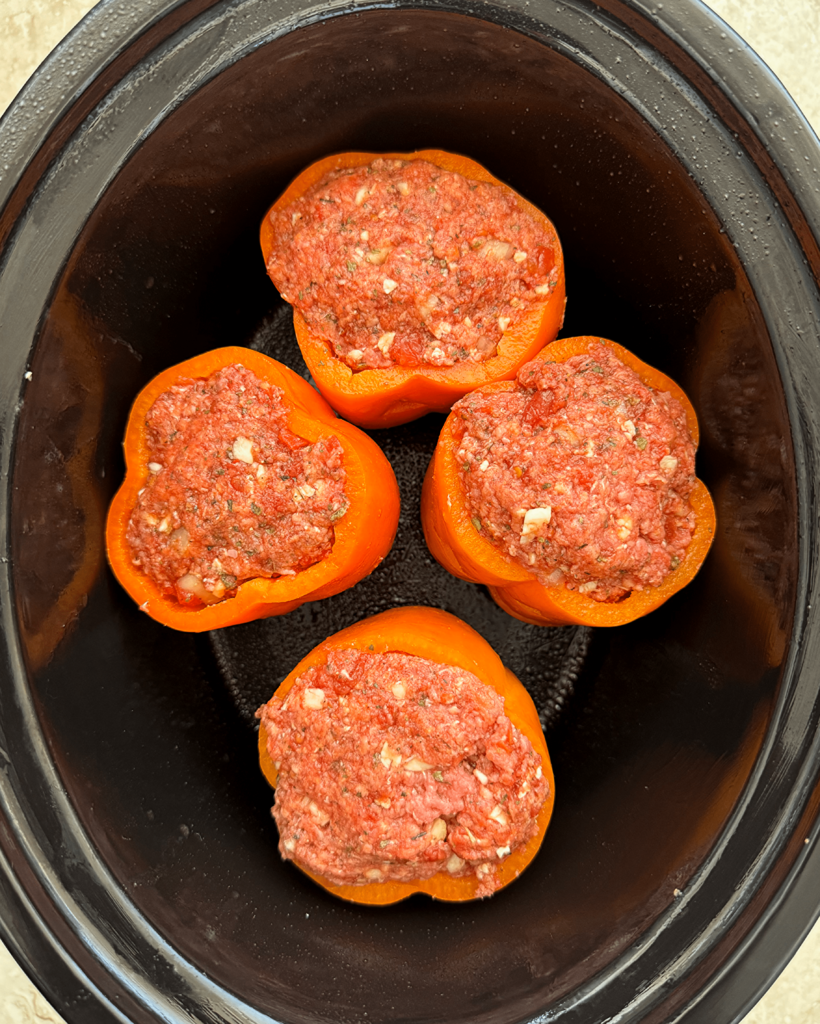 overhead shot of uncooked Jack-O-Lantern Stuffed Peppers in a black slow cooker