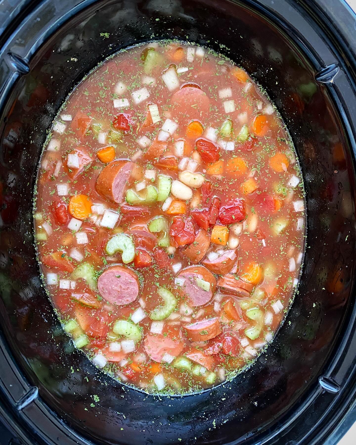 overhead shot of uncooked Crockpot Sausage Bean Veggie Soup n a black slow cooker