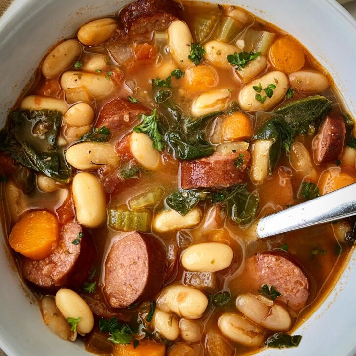 overhead shot of Crockpot Sausage Bean Veggie Soup in a white bowl with a silver spoon