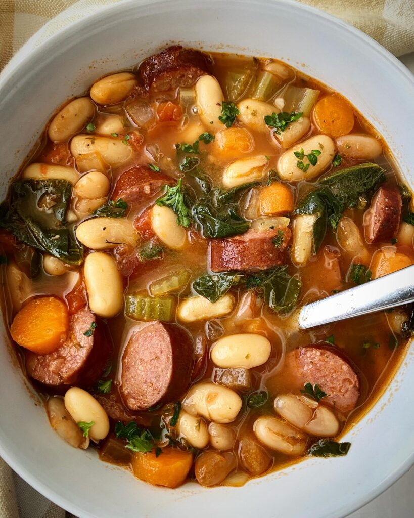 overhead shot of Crockpot Sausage Bean Veggie Soup in a white bowl with a silver spoon